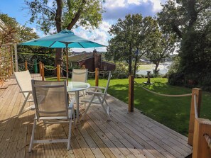An outdoor deck with a table and chairs, a blue umbrella, and a view of a lake and buildings in the background. - 2 bedroom accommodation in Wootton Bridge (Wootton Bridge)