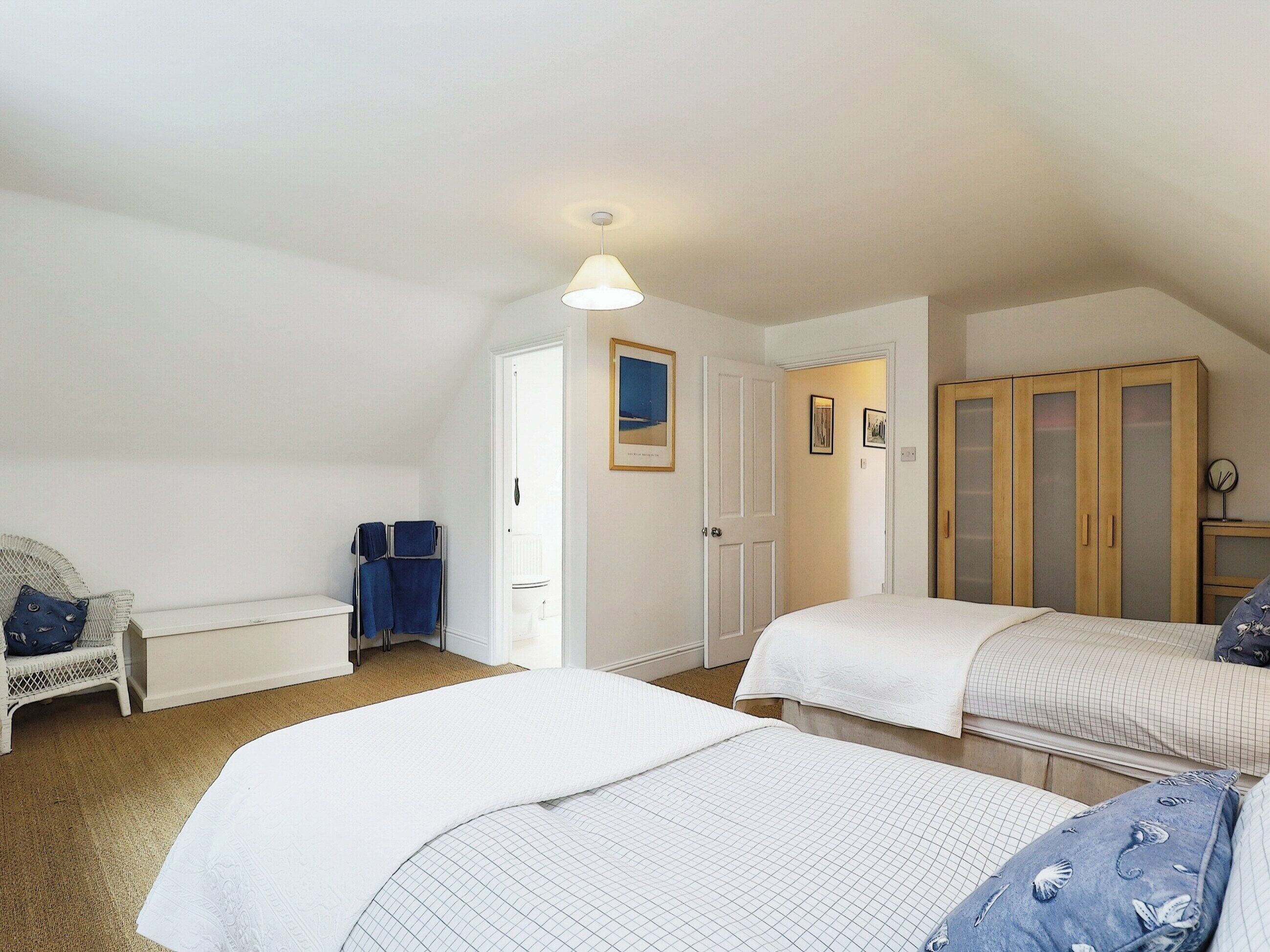 A bedroom with two beds, a wardrobe, a chair, and a door leading to a bathroom.