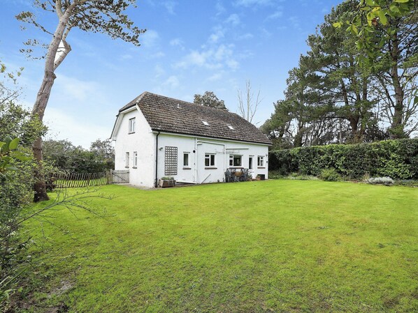 Une maison blanche avec un toit en tuiles, entourée d’une pelouse bien entretenue et d’arbres.