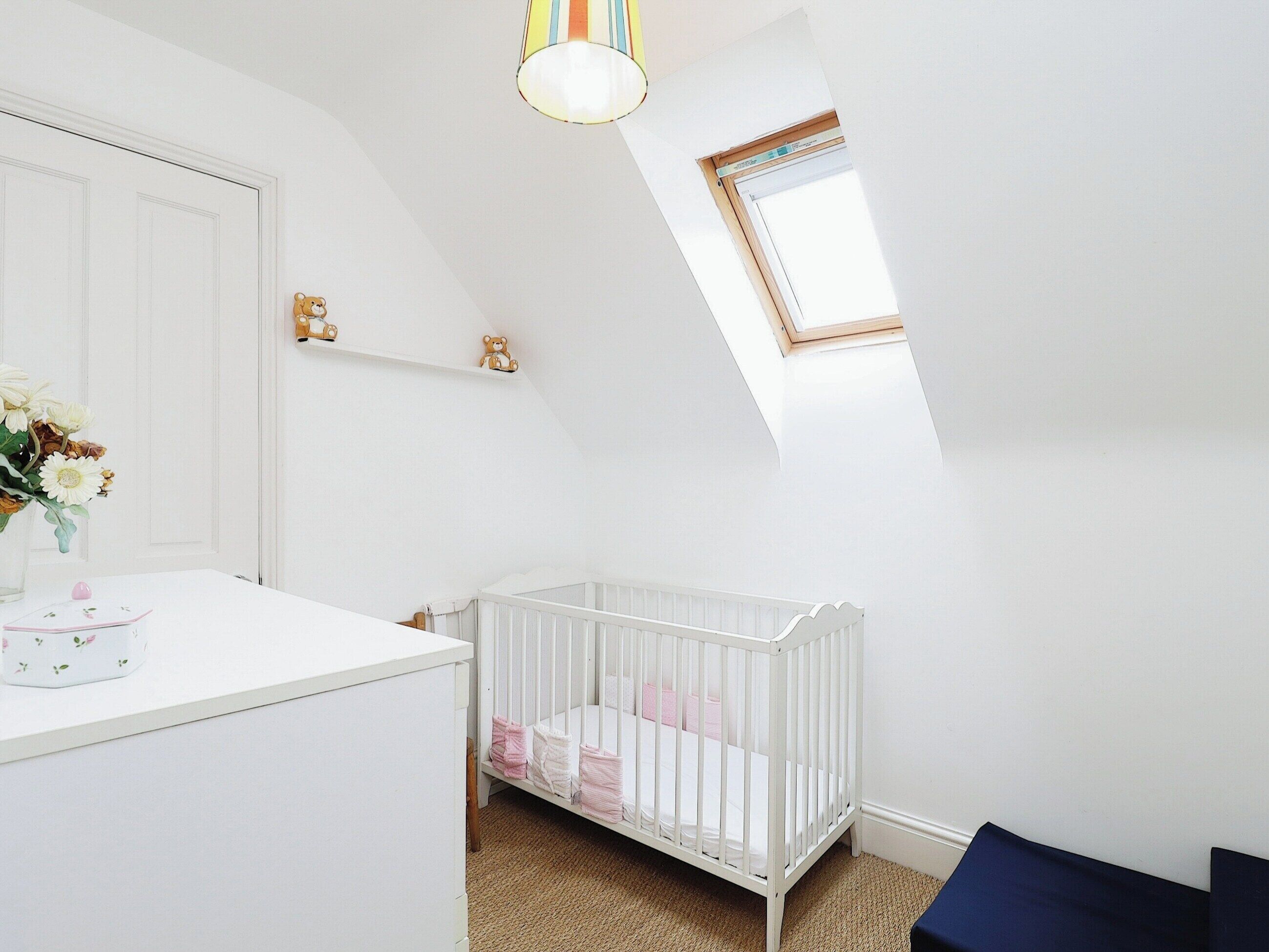 A white room with a crib, a small window, and a mirror.