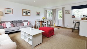 A living room with a sofa, a red ottoman, a white coffee table, and a dining area with a table and chairs.