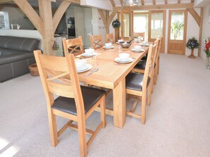 A dining area with a wooden table set for six, surrounded by wooden chairs with black cushions. - 4 bedroom accommodation in Bembridge (Bembridge)