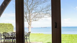 Eine Terrasse mit Tisch und Stühlen, ein Baum und der Blick auf das Meer mit einem Schiff in der Ferne.