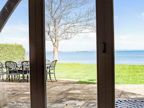 Un patio con una mesa y sillas, un árbol y vista al mar con un barco a lo lejos.