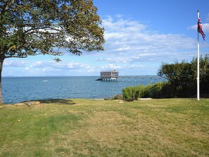 A grassy area with a flagpole and a building on stilts over water. - 4 bedroom accommodation in Bembridge (Bembridge)