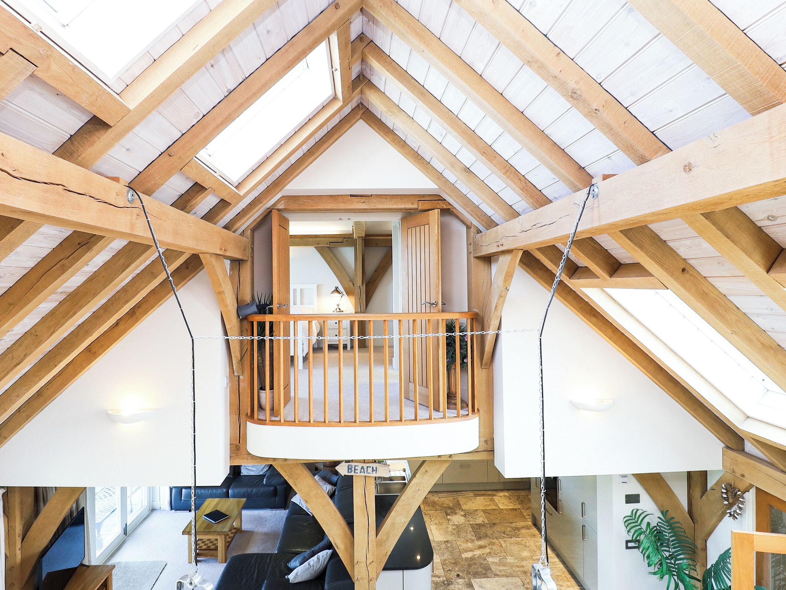 A loft-style bedroom with a wooden balcony, a view of the living area below, and a sign reading "BEACH".