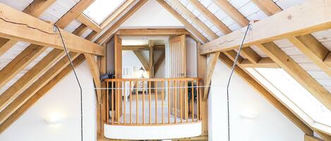 A loft-style bedroom with a wooden balcony, a view of the living area below, and a sign reading "BEACH".