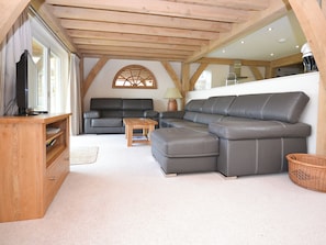 A cozy living room with a wooden ceiling, a black leather sofa, a wooden coffee table, and a television on a wooden stand.