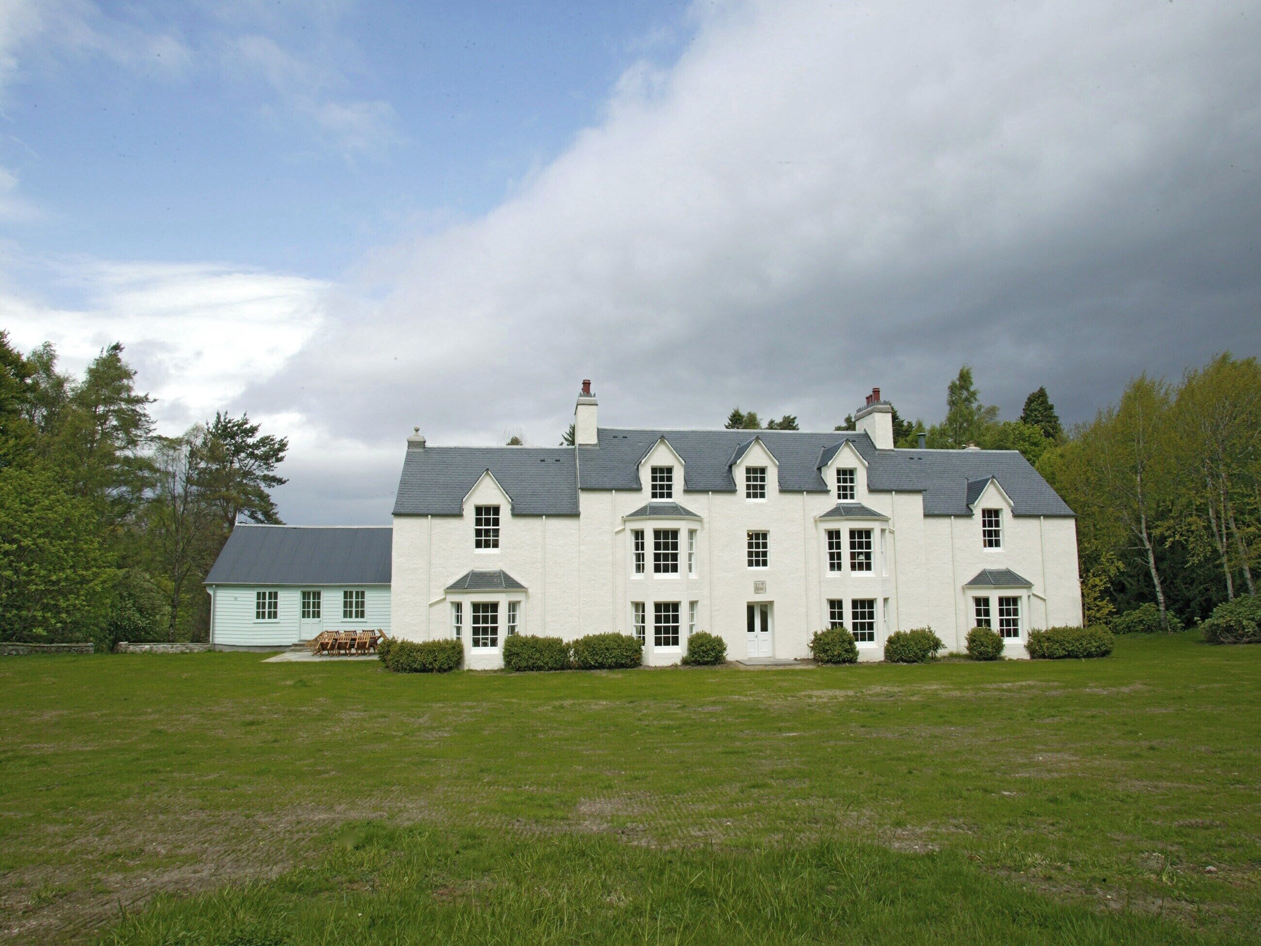 Un grand bâtiment blanc, à plusieurs étages, doté d’une façade symétrique, de nombreuses fenêtres et d’une pelouse verdoyante à l’avant.