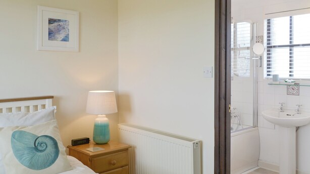 A bedroom with a bed, bedside lamp, and a view into the bathroom. - 1 bedroom accommodation in Pelynt, near Looe (Pelynt, near Looe)