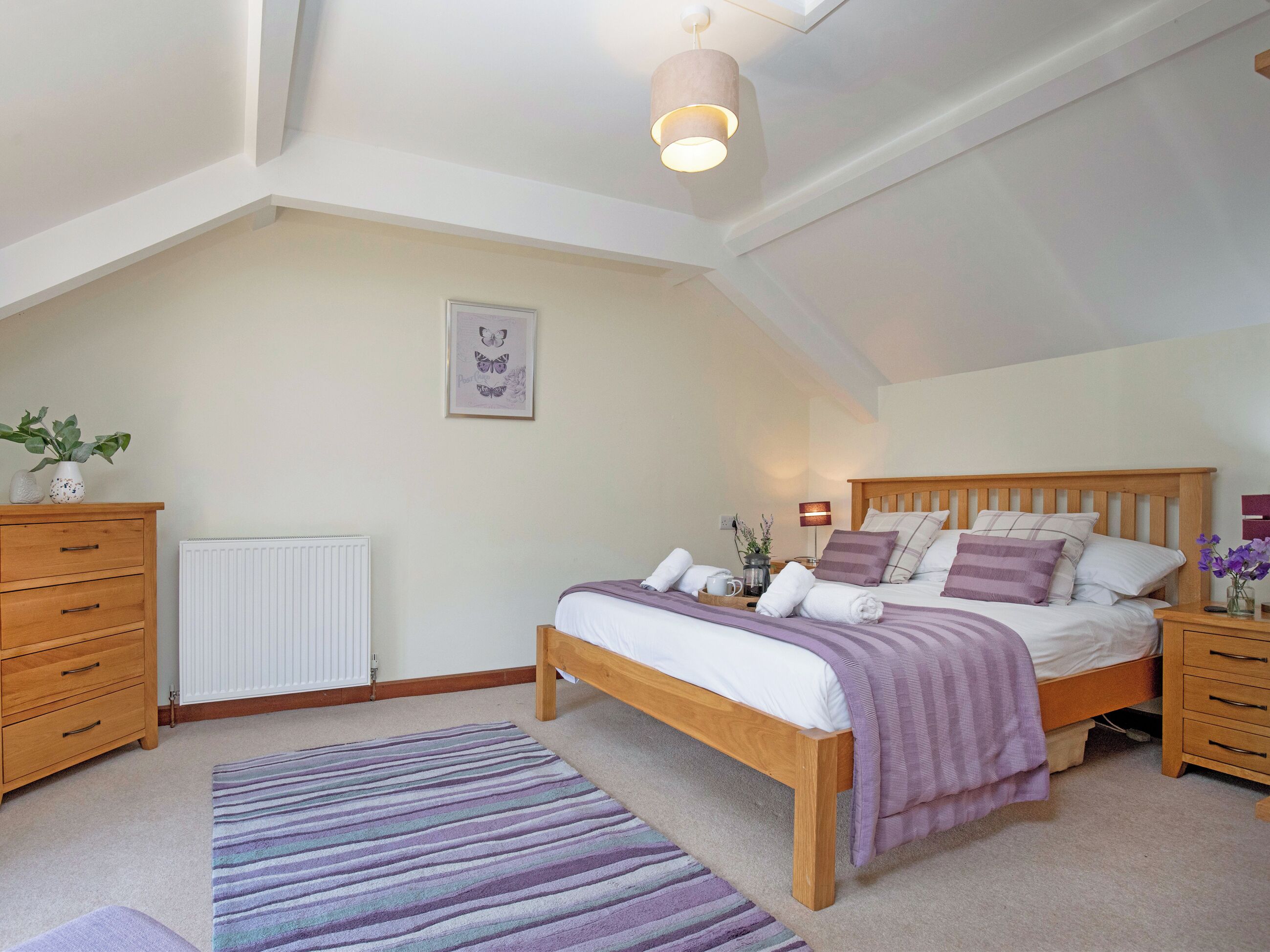 A bedroom with a bed, wooden dresser, radiator, and a ceiling light fixture.
