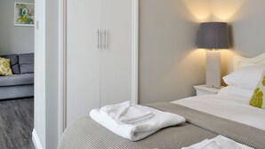 Habitació d'hotel amb un llit, una tauleta de nit, una làmpada, un armari i un sofà gris.