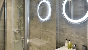 Un bany modern amb dutxa protegida per vidre, un lavabo amb mirall i dos miralls il·luminats.