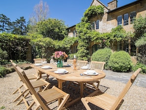 Un espace extérieur aménagé pour les repas, avec une table ronde en bois, six chaises en bois et un vase rempli de fleurs.