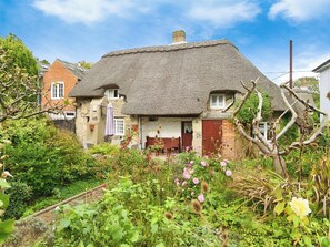A traditional thatched-roof cottage with a garden in front.