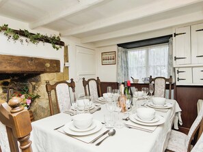A dining room with a white table set for four, wooden chairs, a stone fireplace, and a window with curtains.