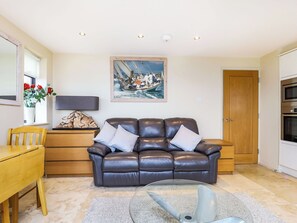 A living room with a leather sofa, a glass coffee table, a wooden side table, a painting of a boat, and a wooden door. - 1 bedroom accommodation in Cowes (Cowes)