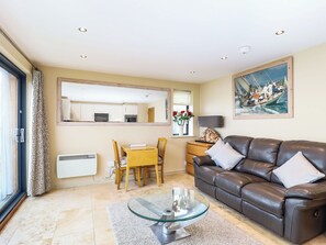 A living room with a brown leather sofa, a glass coffee table, a dining area with a yellow table and chairs, a large mirror, and a painting of a boat on the wall. - 1 bedroom accommodation in Cowes (Cowes)
