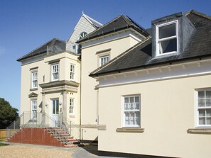 A two-story building with a symmetrical facade, a central entrance with a staircase, and a small balcony on the second floor. - Highlands Apartment 2 - UKC2900 (Shanklin)