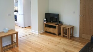 Un soggiorno con pavimento in legno, una TV su un mobile in legno, un tavolino e una porta.