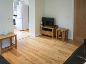 A living room with a wooden floor, a TV on a wooden stand, a small table, and a door. - Highlands Apartment 2 - UKC2900 (Shanklin)