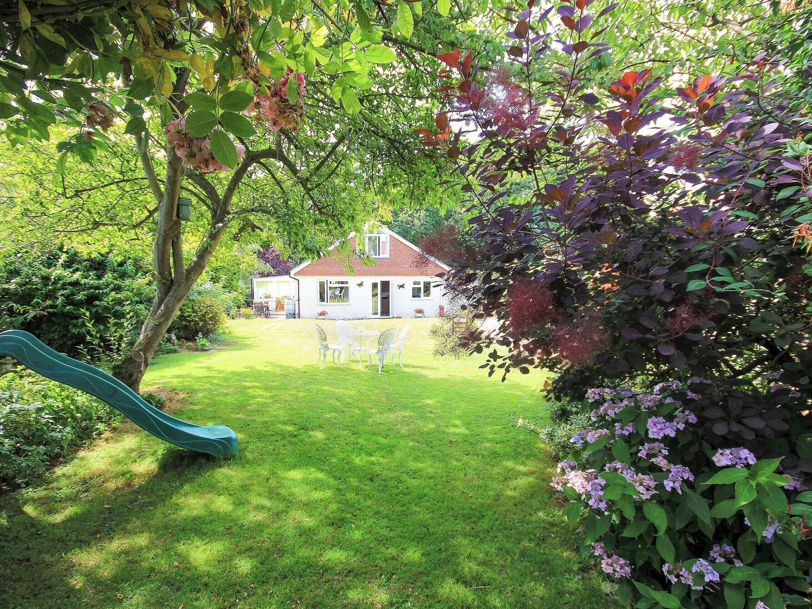 A house with a visible front yard, a slide, and a garden with various plants.