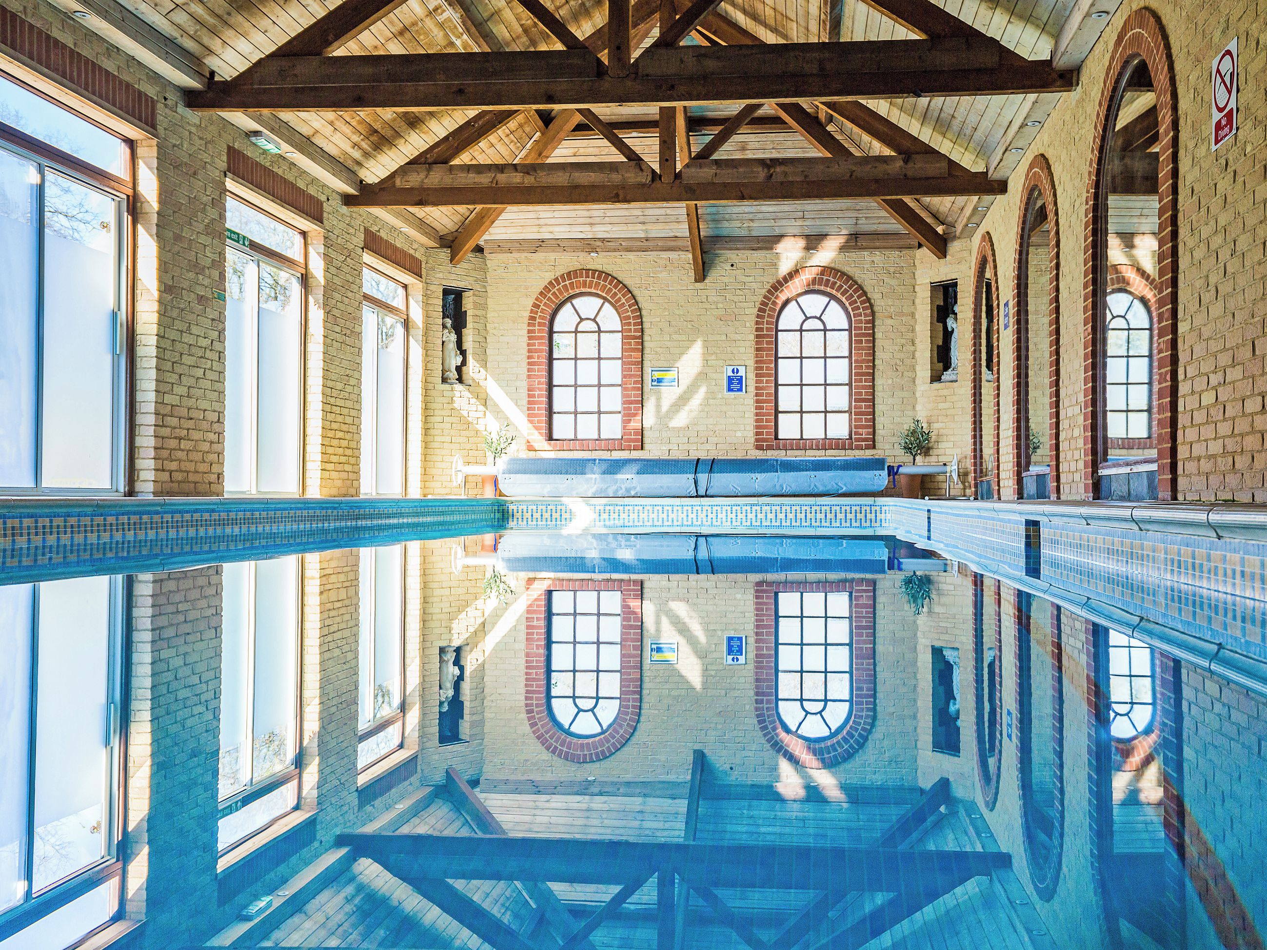 Una piscina interior con reflejos nítidos, vigas de madera y ventanas arqueadas.