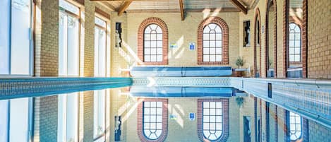 Una piscina interior con reflejos nítidos, vigas de madera y ventanas arqueadas.
