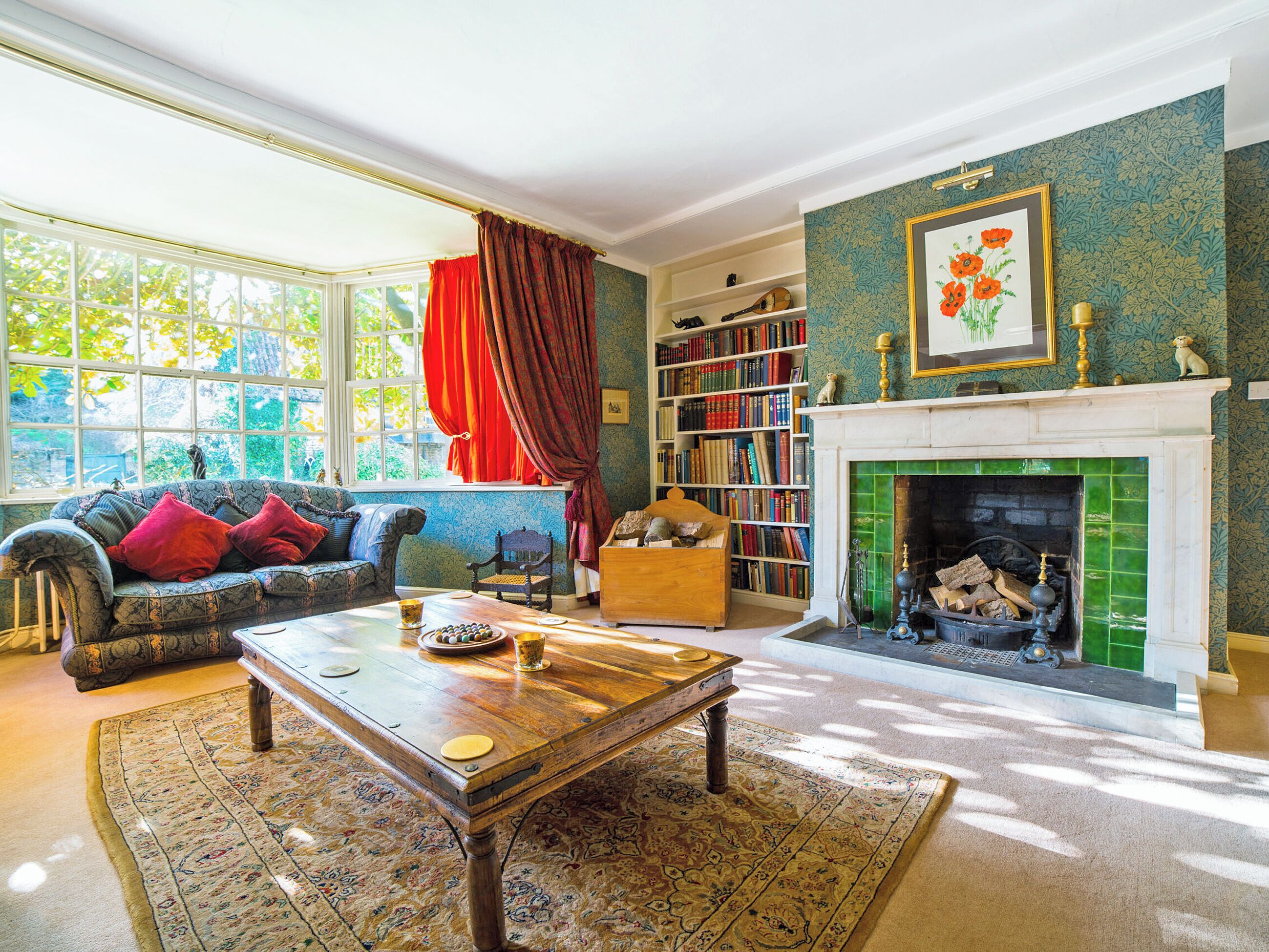 A cozy living room with a fireplace, a bookshelf, and a large window.