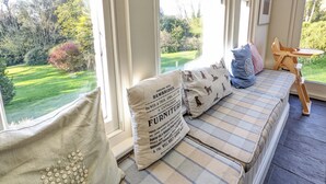 A cozy seating area with a view of a lush garden, featuring a bench with striped cushions and decorative pillows. - 6 bedroom accommodation in Brading, near Sandown (Brading, near Sandown)