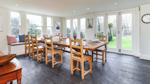 A dining area with a wooden table and chairs, large windows, and a view of the garden. - 6 bedroom accommodation in Brading, near Sandown (Brading, near Sandown)
