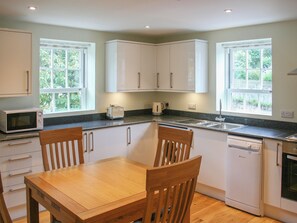 A kitchen with white cabinets, a wooden dining table, and two windows. - Highlands Apartment 3 - UKC3105 (Shanklin)