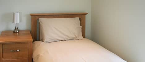 A small, neatly made bed with a wooden headboard, a bedside table with a lamp, and a drawer unit.