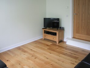 A room with a wooden TV stand, a flat-screen TV, and a wooden door. - Highlands Apartment 3 - UKC3105 (Shanklin)