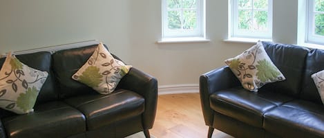 Una habitación con dos sofás de cuero oscuro, cada uno con cojines estampados, frente a una pared con dos ventanas.