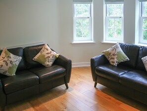 A room with two dark leather sofas, each with patterned cushions, positioned against a wall with two windows. - Highlands Apartment 3 - UKC3105 (Shanklin)