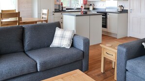 A modern kitchen with white cabinets, a central island, and a dining area with a wooden table and chairs. - 2 bedroom accommodation in Forres, near Nairn (Forres, near Nairn)