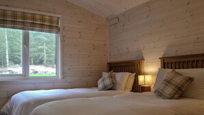 A bedroom with two beds, wooden walls, a window with a plaid blind, and a nightstand with a lamp. - 2 bedroom accommodation in Forres, near Nairn (Forres, near Nairn)