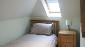 Un dormitorio con techo inclinado, una cama individual con cabecera de madera, una mesita de noche con lámpara y un pequeño aparador de madera.