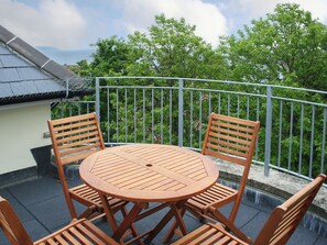Een ronde houten tafel met vier stoelen op een balkon met een metalen hekwerk.