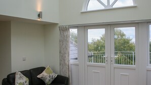Una habitación con un sofá de cuero negro, dos almohadones decorativos, una puerta blanca con paneles de vidrio y vistas a zonas verdes.