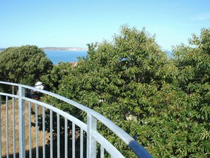 Ein Balkon mit Blick auf eine Küstenlandschaft, Bäume und einen klaren, blauen Himmel.