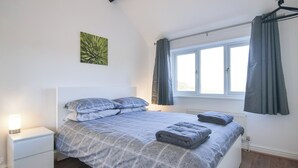 Een slaapkamer met een groot bed, een nachtkastje, een raam met gordijnen en een radiator.