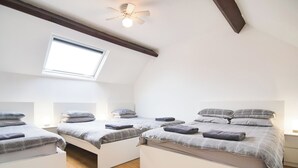 Habitación con tres camas, tragaluz, ventilador de techo y suelo de madera.