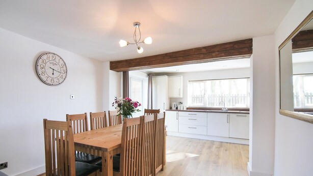 A modern kitchen with white cabinets, a wooden dining table with chairs, and a large window. - 2 bedroom accommodation in Murton, near York (Murton, near York)