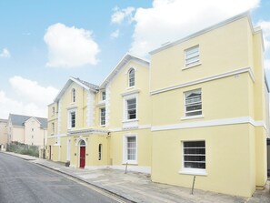 A row of yellow buildings with white trim, a red door, and multiple windows. - This second floor holiday apartment is close to the heart of Torquay. (Torquay)