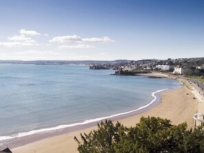 Blick auf die Küste mit einem Sandstrand, ruhiger See und einer Stadt im Hintergrund.