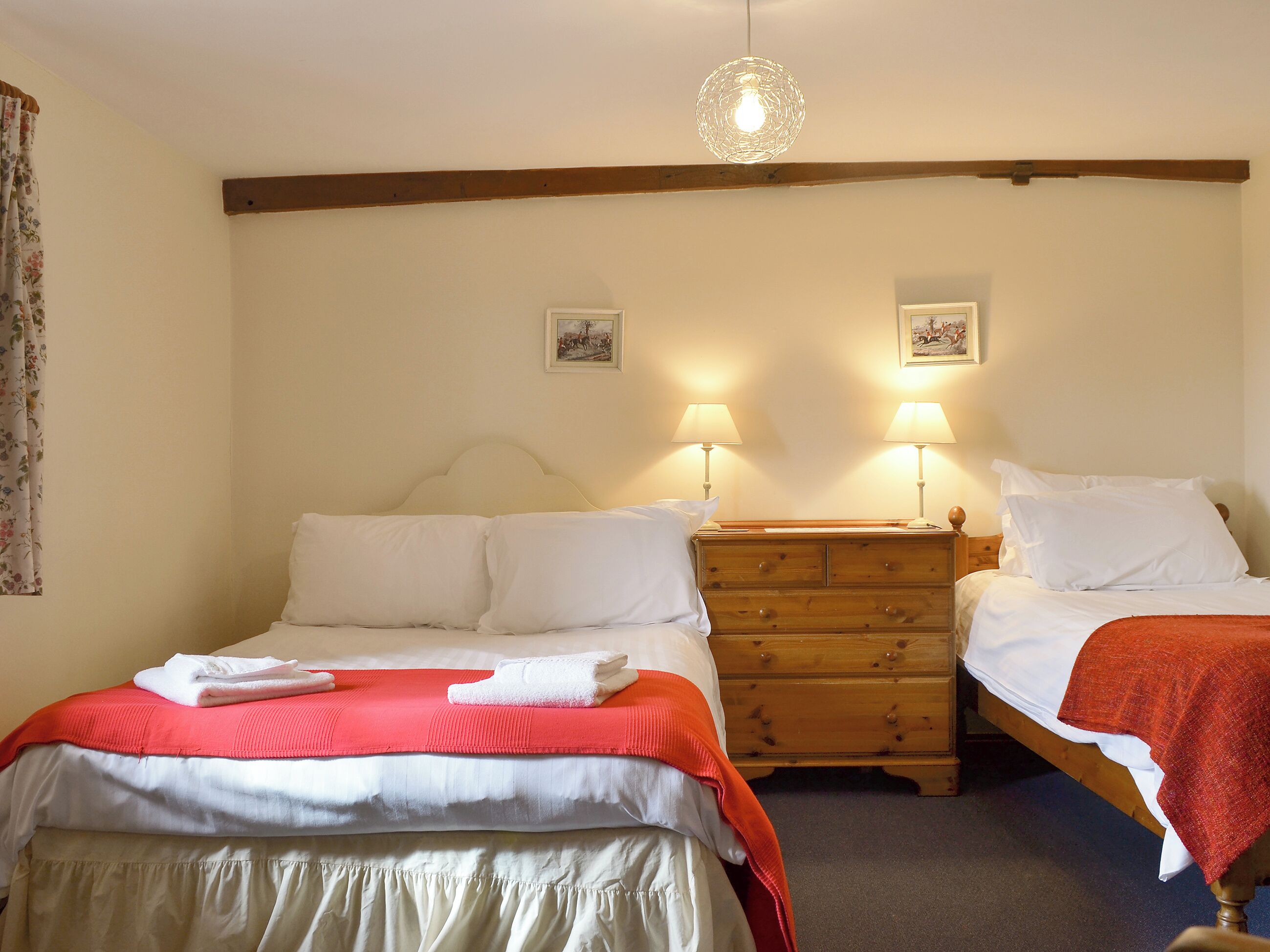 A bedroom with two beds, a wooden dresser, and two wall-mounted lamps.