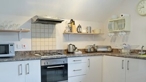 Una cuina moderna amb armaris blancs, fogó a gas, microones i torradora.