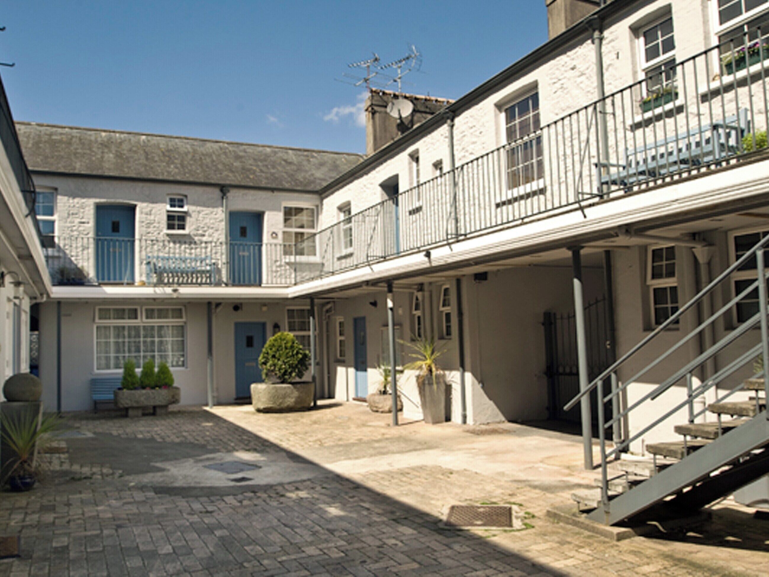 A courtyard with a stone floor, potted plants, and a staircase leading to an upper level.